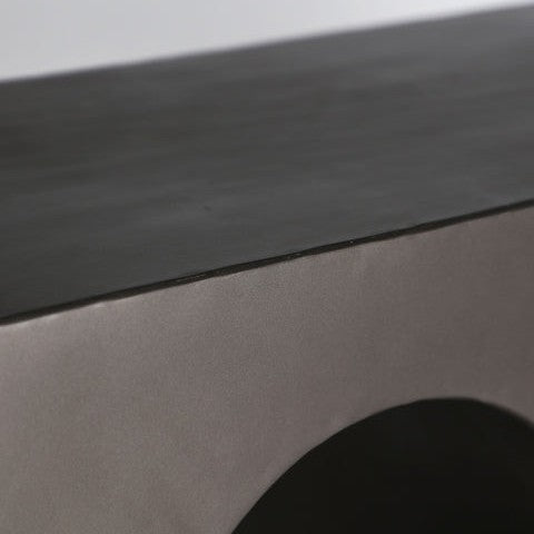 Un primer plano de la Consola en hierro Industrial Rethel, con una parte superior negra y un recorte en forma de arco en su base de color claro, resalta su estilo contemporáneo y su elegante acabado industrial.