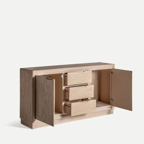 El Aparador en madera DM (150x38x80 cm) Werle presenta un acabado natural con puertas texturizadas que revelan tres cajones interiores, ofreciendo almacenamiento práctico y haciendo eco de un sutil diseño Art Deco, aportando sofisticación y utilidad a cualquier habitación.