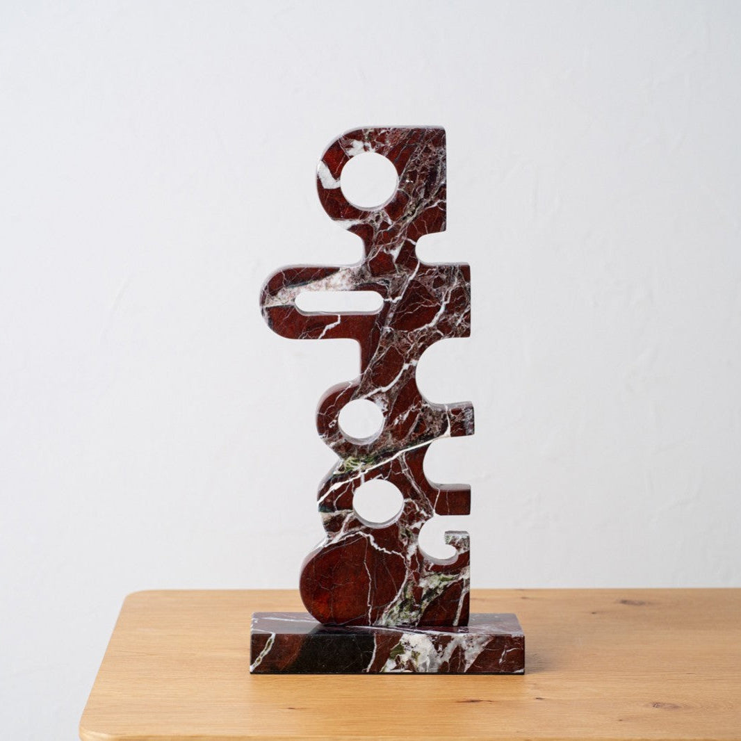 La Figura decorativa abstracta en mármol Stelio presenta un diseño geométrico de mármol con recortes, ideal para exhibir arte contemporáneo y aportar sofisticación a cualquier espacio sobre una superficie de madera.