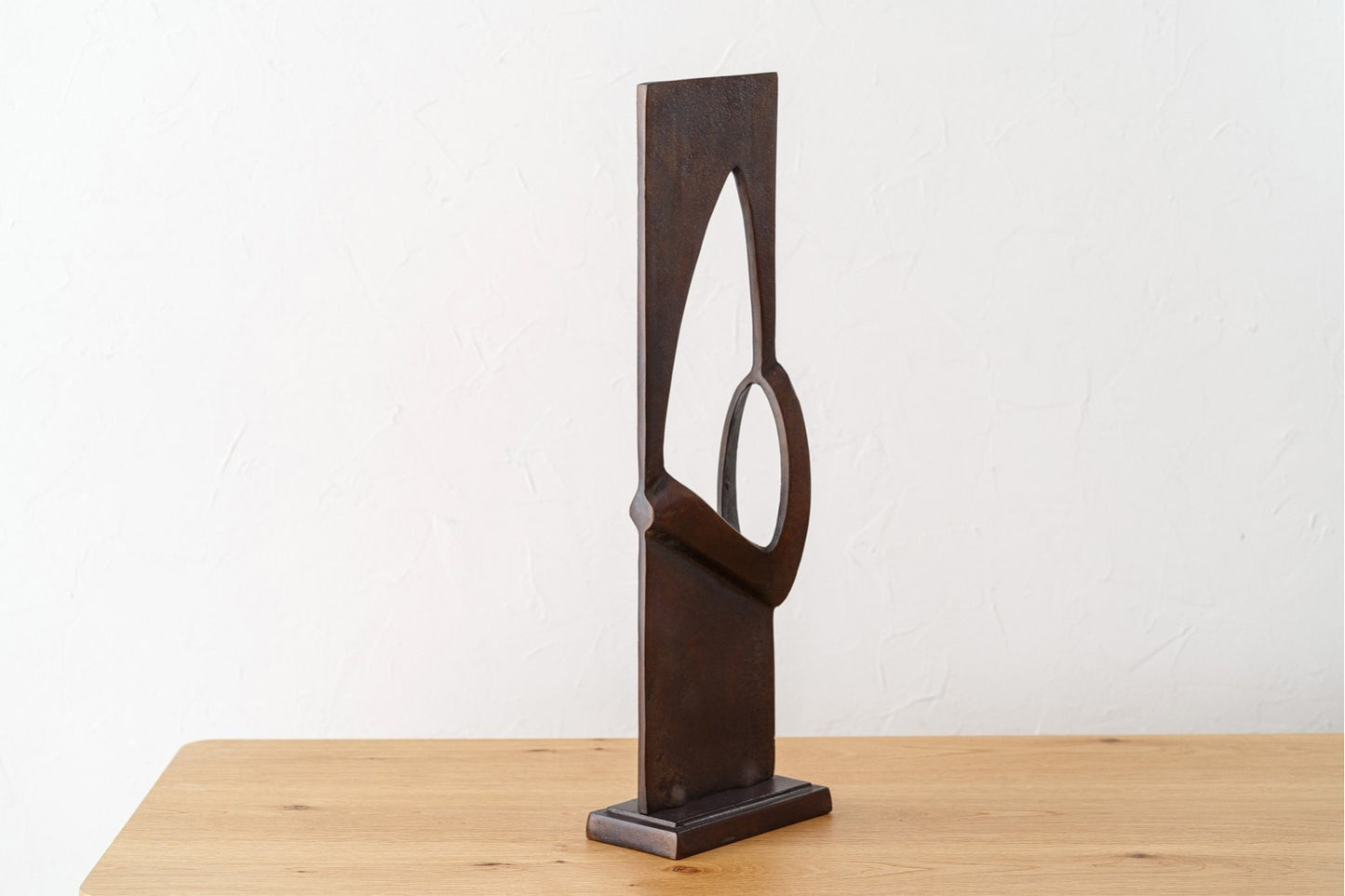 La Escultura abstracta de metal con acabado óxido envejecido - moderna - DOOR se alza sobre una superficie de madera frente a una pared blanca texturizada, ideal para decoración moderna.