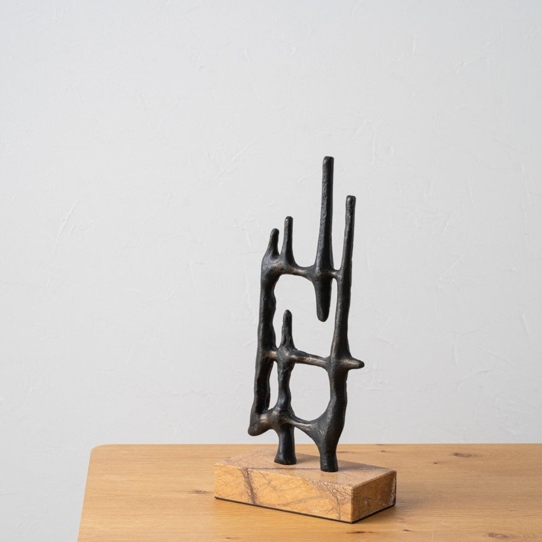 La Escultura en metal y mármol Abstracta N4 presenta varillas que se cruzan sobre una base de madera rectangular, exhibidas sobre una mesa de madera clara contra una pared blanca, ideal para decoración exclusiva y un toque de diseño contemporáneo.
