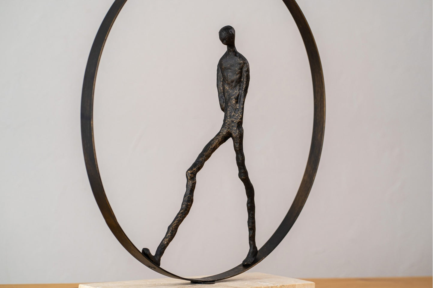 La Escultura de metal - mármol - bronce envejecido - moderna CAMINANDO EN CIRCULO presenta una figura humana decorativa minimalista caminando dentro de un marco circular, ideal para exponer sobre superficies de madera clara.