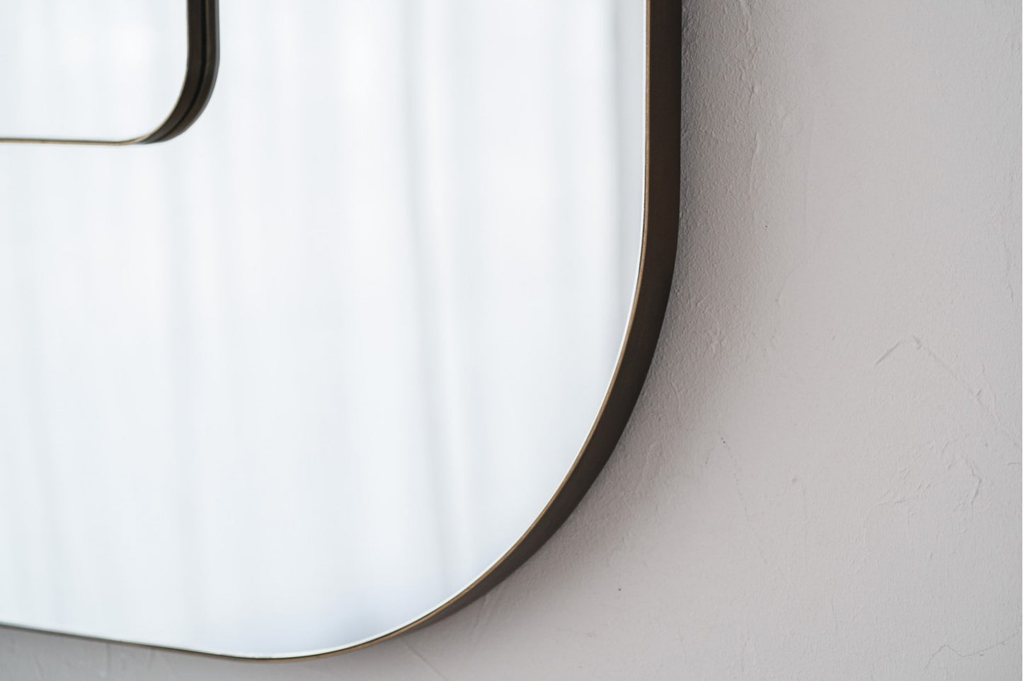 Primer plano del CUADRADO DOBLE espejo de pared cuadrado doble de metal (89×4×89 cm) en oro envejecido, montado sobre una pared blanca. Los suaves reflejos y su moderno marco de metal dorado envejecido aportan elegancia al espacio.