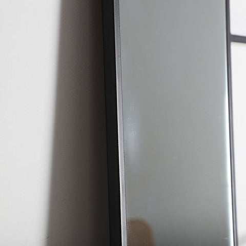 Una vista cercana del borde del Espejo rectangular en hierro negro (66x180 cm) Ezequiel montado sobre una pared de color claro, complementando el diseño contemporáneo y el ambiente industrial del espacio.