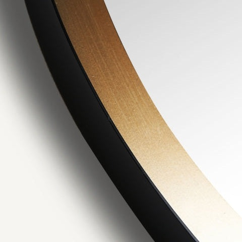 Primer plano del borde de un espejo circular de hierro y madera Jacou, con marco negro y dorado con elegante diseño art decó, sobre un fondo blanco.