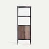La Estantería en hierro con armario Elstob, alta y negra, tiene dos estantes abiertos superiores y un armario inferior con puertas de ratán tejido y tiradores metálicos, fusionando elegancia industrial y diseño contemporáneo.