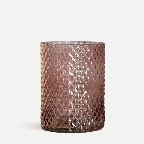 Un vaso de vidrio transparente con patrón de diamantes, que recuerda al estilo del Jarrón en vidrio marrón Juke, presenta su elegante textura sobre un fondo claro y simple, ideal para la decoración contemporánea.