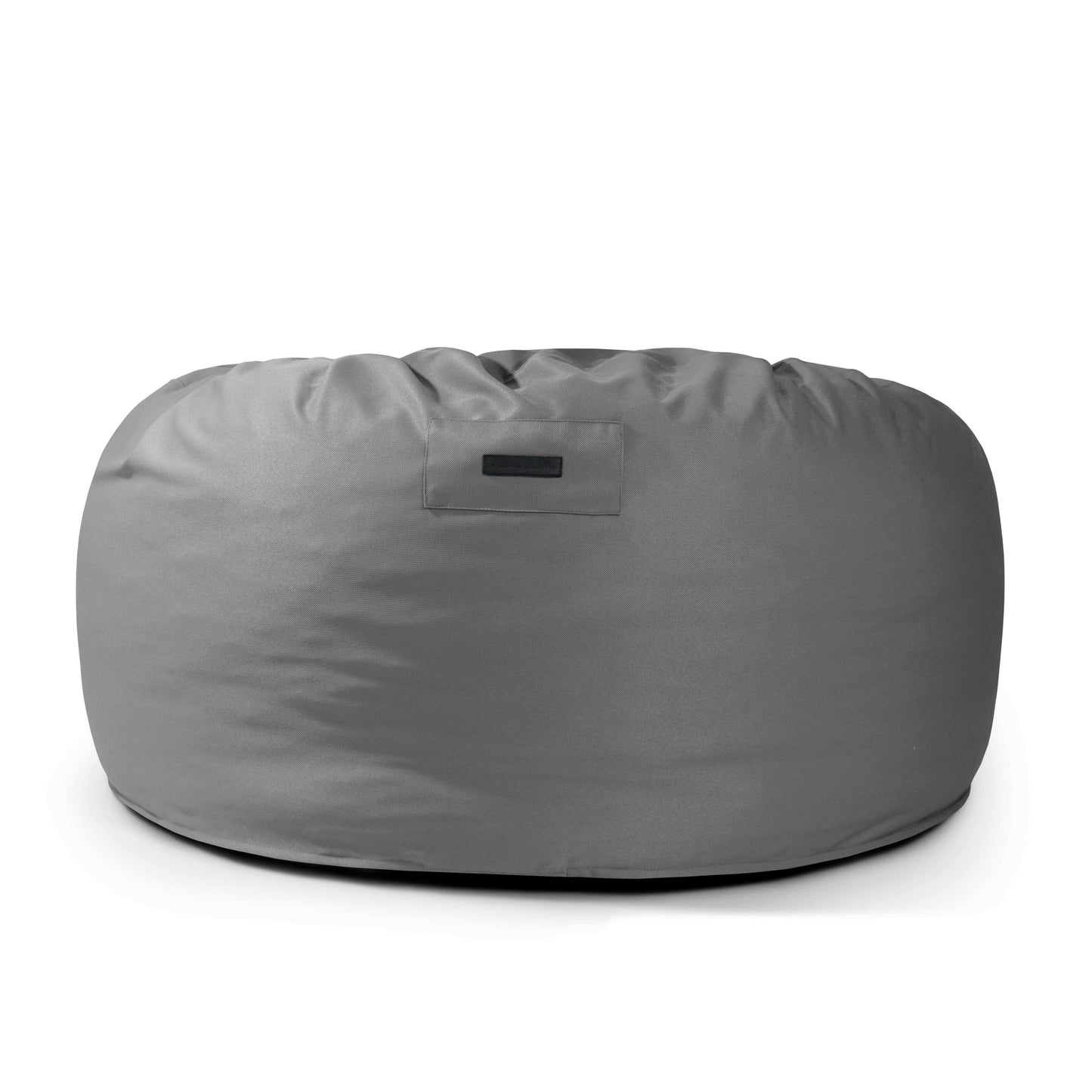 El Foam Bean Bag OM 110 Barcelona es un bean bag grande y redondo de color gris con superficie de tela lisa, relleno de copos de espuma de alta densidad y con una pequeña etiqueta rectangular en la parte delantera.