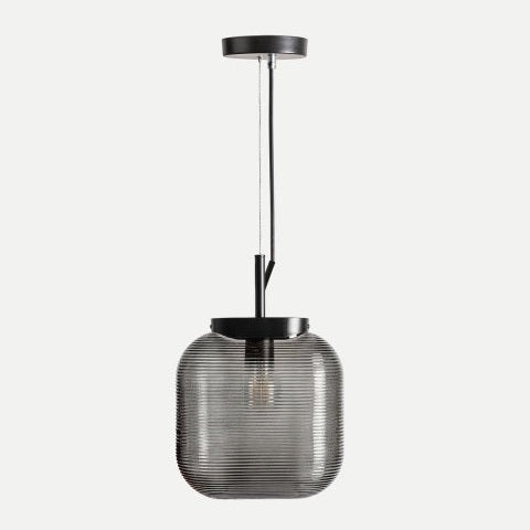 La Lámpara de colgar en vidrio negro Ahumo presenta un diseño minimalista con base metálica negra y pantalla de vidrio acanalado, suspendida por cable negro sobre fondo claro.