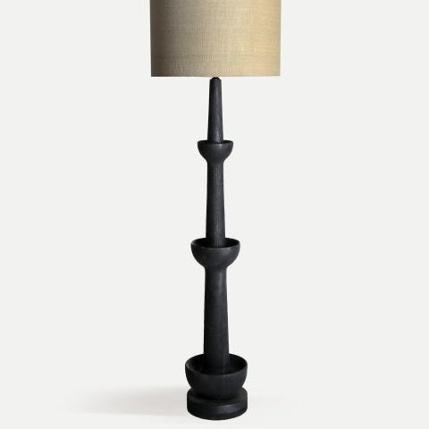 Lámpara de pie en madera de mango Haverslev, negra y alta, con base escultórica escalonada y pantalla cilíndrica beige, perfecta para decoración moderna sobre fondo claro.