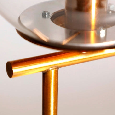 Primer plano de la Lámpara de mesa en hierro y mármol Leba, una obra maestra moderna con una tapa de cristal circular y dos varillas cilíndricas doradas que se entrecruzan y que recuerdan al estilo Art Decó.