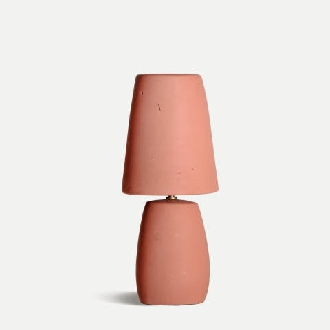 La lámpara de mesa en terracota coral Swahili C, con base cilíndrica y pantalla cónica a juego, destaca sobre fondo claro y se integra perfectamente en cualquier espacio de diseño contemporáneo.