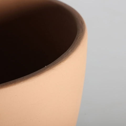 Primer plano del borde y la parte superior de una taza de cerámica marrón claro, lisa y sin esmaltar, sobre un fondo neutro, que evoca el diseño elegante característico de la Lámpara de sobremesa en terracota Swahili C.