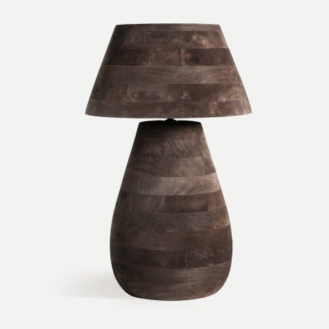 La lámpara de mesa en madera de mango Volsted B presenta pantalla cónica y base redondeada, ambas con acabado estriado oscuro, evocando el estilo colonial sobre fondo claro.