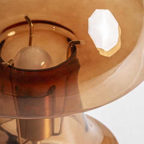 Primer plano de la Lámpara de sobremesa en vidrio ámbar Lumik, que presenta una pantalla de vidrio ámbar marrón con un chip blanco visible y que muestra la bombilla interna y el accesorio de metal dorado.