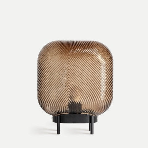 La lámpara de mesa en vidrio marrón Espiga, de forma cuadrada con textura diagonal y base metálica negra, aporta iluminación cálida en cualquier espacio sobre un fondo claro.