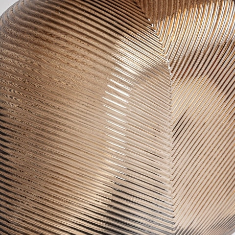 Primer plano de la superficie de vidrio marrón de la lámpara de mesa en vidrio marrón Espiga, que presenta ranuras curvas y paralelas en tonos dorados y bronce para una apariencia contemporánea ideal para una iluminación ambiental cálida.
