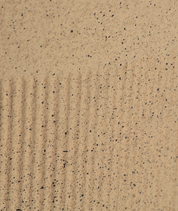 Primer plano de arena fina, que recuerda el aspecto de la arena de color Macetero de poliresina 40×40×91 cm KAVAN, con líneas paralelas uniformemente espaciadas a la izquierda y motas oscuras dispersas por la superficie.