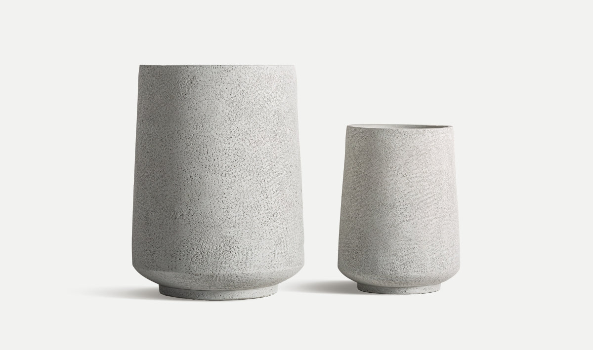 El juego de 2 maceteros de cerámica gris NOVA, de diseño minimalista y forma cilíndrica en diferentes alturas, se muestra junto sobre un fondo blanco.