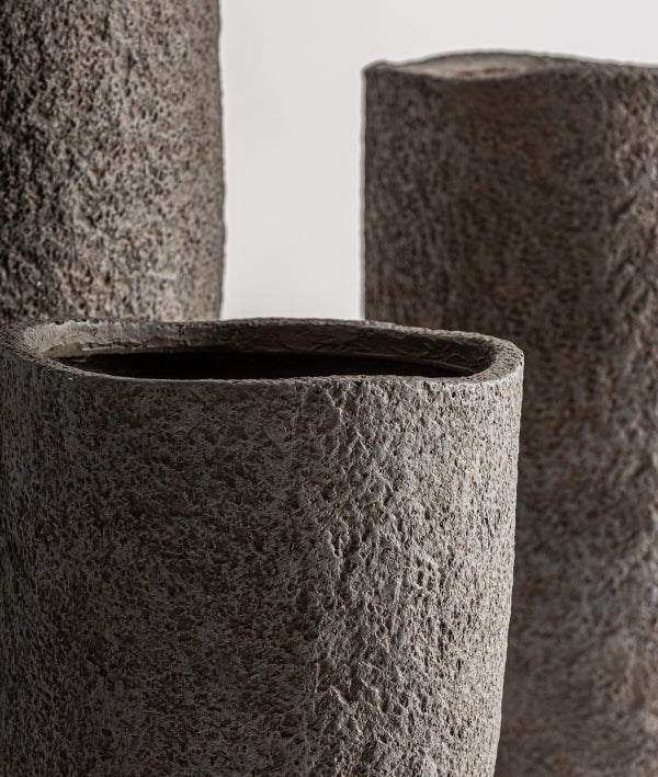 Primer plano de tres maceteros altos Juego de 3 maceteros de cerámica gris rugosa - natural - ROKA, sus formas cilíndricas presentan superficies rugosas y texturadas sobre un fondo liso.