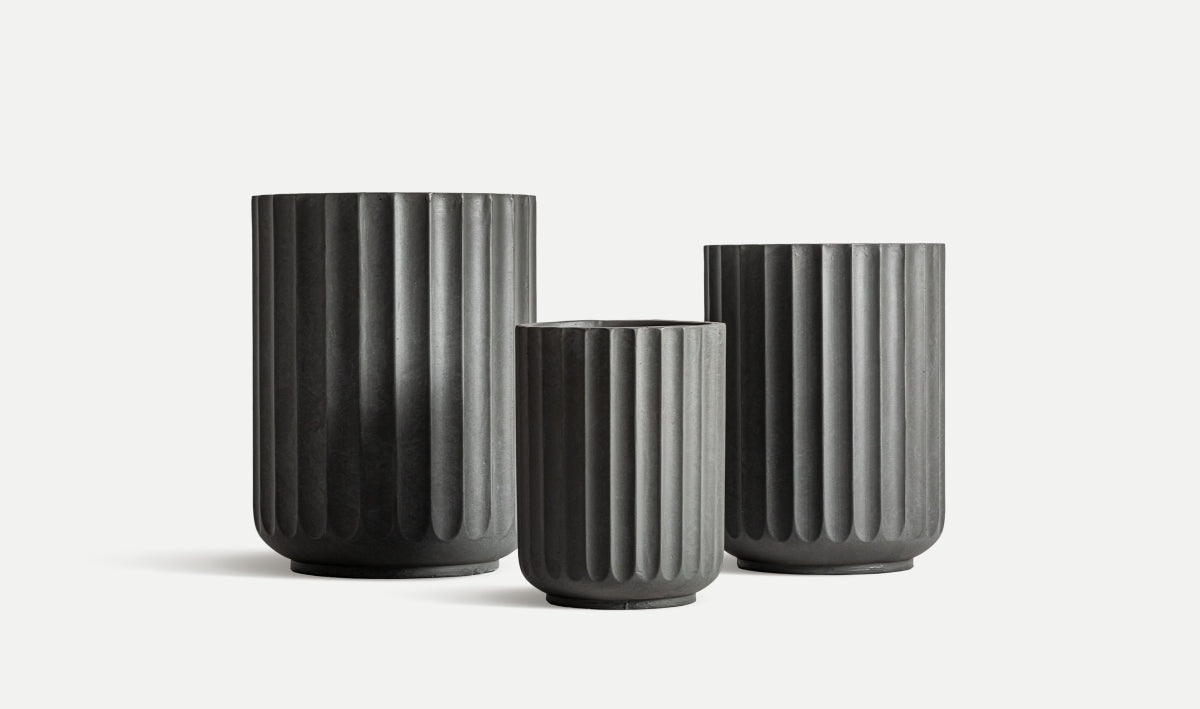 El juego de 3 maceteros de cerámica estriada gris TAVO, en diferentes alturas, está dispuesto lado a lado sobre un fondo blanco, resaltando su diseño contemporáneo.