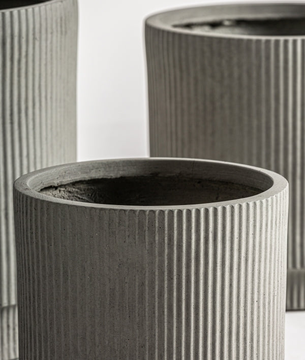 El Juego de 3 maceteros de cerámica estriada gris - natural VULK, con diseño cilíndrico y líneas verticales, es ideal para aportar un toque contemporáneo a cualquier proyecto de interiorismo.