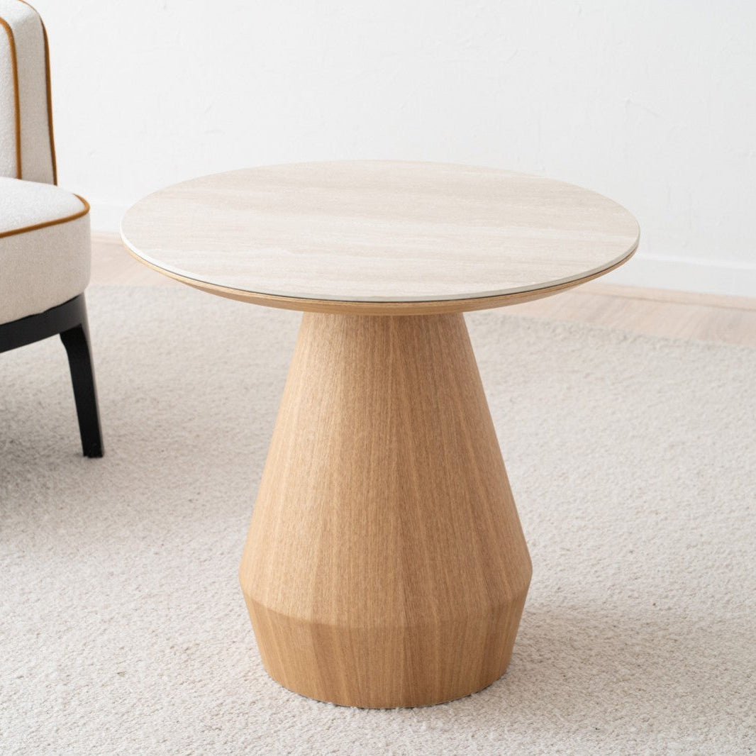 Una Mesa Auxiliar en Fresno y Cerámico Beige Frelia Ø60 reposa sobre una alfombra clara junto a una silla beige con pata negra, mostrando un diseño moderno.