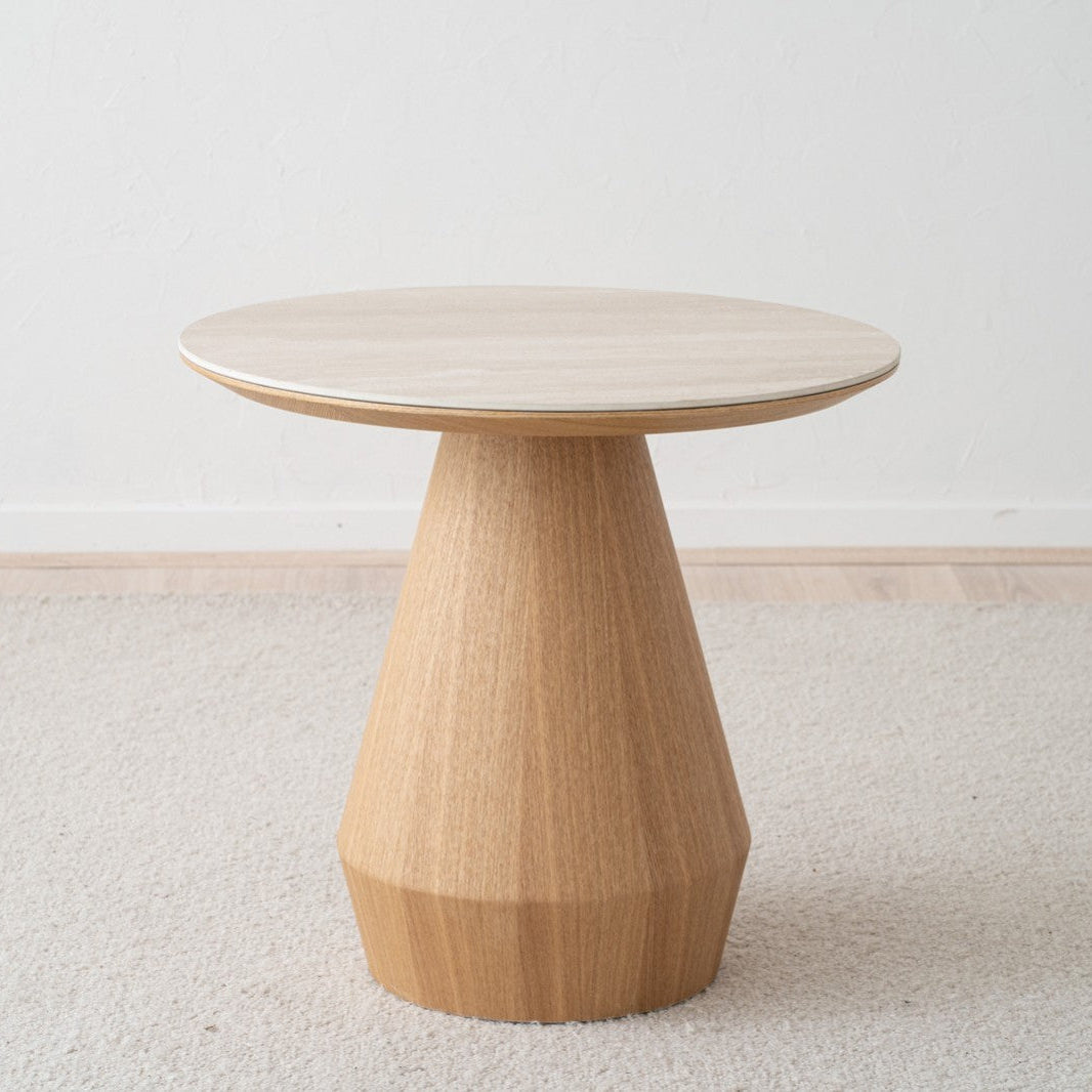 La Mesa auxiliar en Fresno y Cerámico Beige Frelia Ø60, con su diseño moderno y base cónica, se alza sobre una alfombra beige en una estancia minimalista.