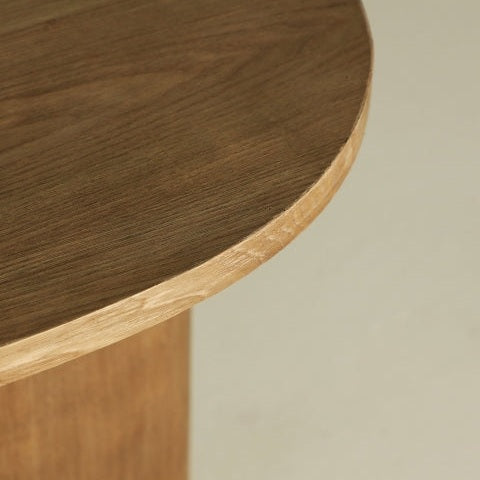Un primer plano de la Mesa Auxiliar Redonda de Abeto Hoek1 revela un diseño sencillo y redondeado en madera de abeto. Su llamativa textura veteada y su acabado liso realzan su estética moderna, mientras que parte de una pata de la mesa se aprecia sutilmente al fondo.