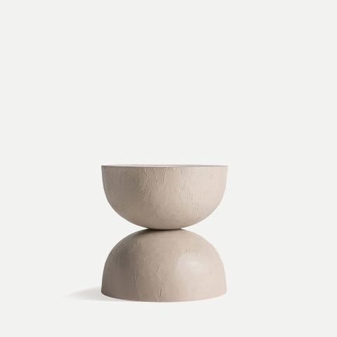 Un taburete minimalista y redondo en beige con acabado texturizado presenta dos semiesferas apiladas. Se asienta elegantemente sobre un fondo liso y claro. Este diseño versátil encarna el estilo moderno, convirtiéndolo en la mesa auxiliar de arcilla con detalles DM Kotka perfecta para espacios contemporáneos.