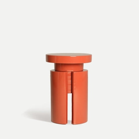 Un taburete cilíndrico moderno de color naranja con ranuras verticales destaca como Mesa auxiliar en hierro rojo Lausana sobre un fondo blanco liso.