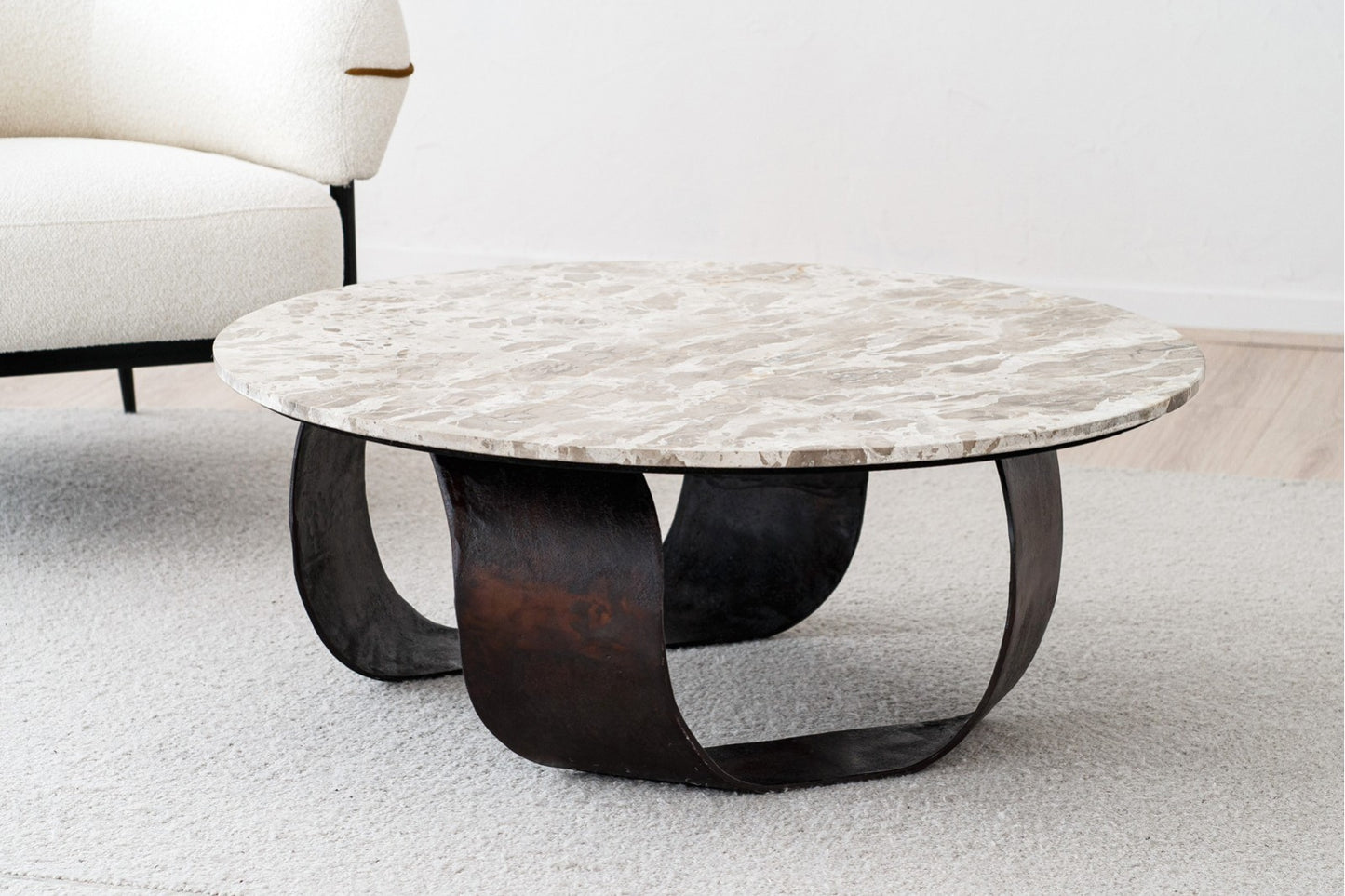 La mesa de centro redonda de metal y mármol MAYA (100×38 cm) destaca sobre una alfombra clara junto a una silla blanca tapizada, aportando un toque elegante y contemporáneo al espacio.