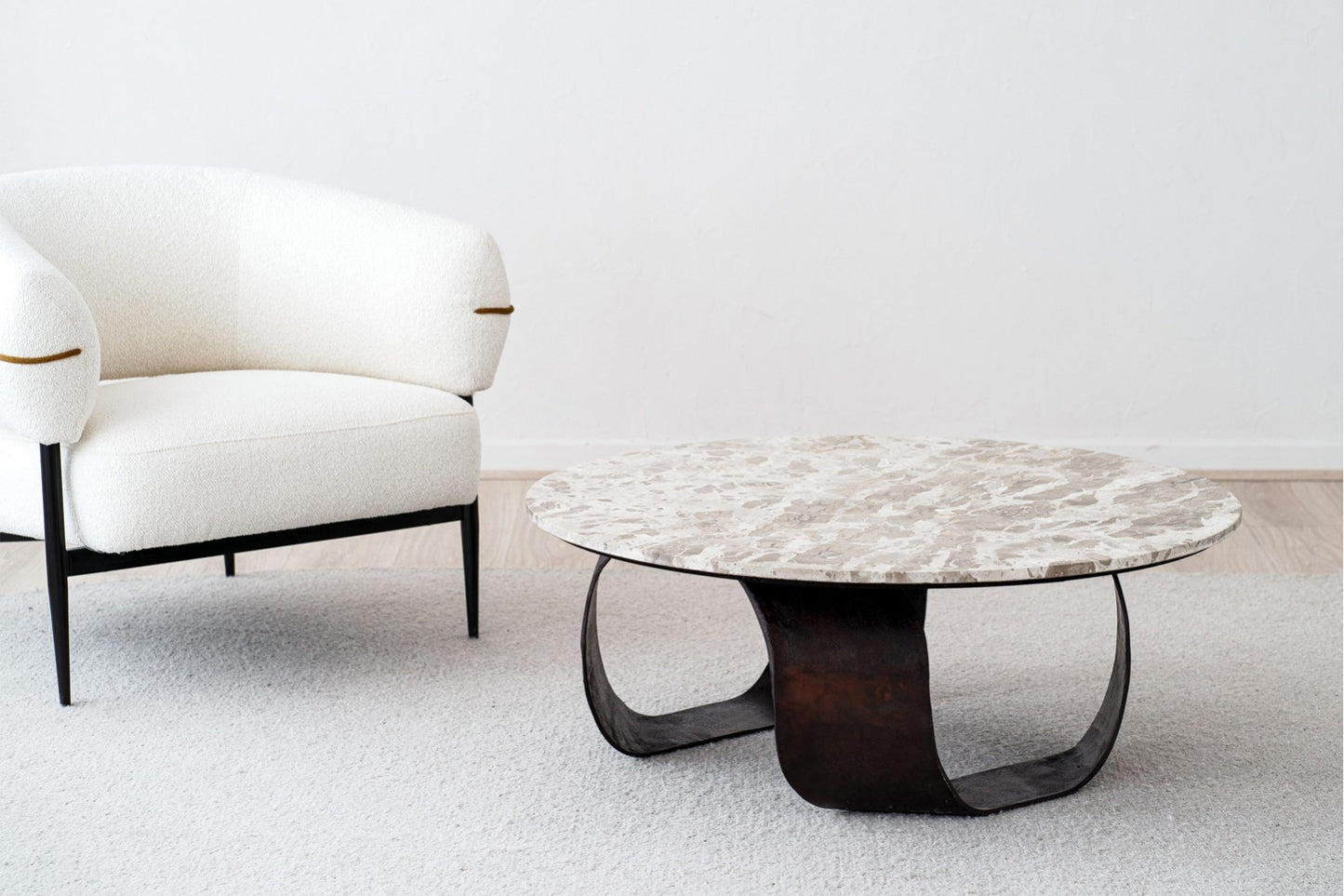 Un moderno sillón blanco y la mesa de centro redonda contemporánea MAYA de metal con tablero de mármol de 100×38 CM se alzan sobre una alfombra clara en un salón minimalista.