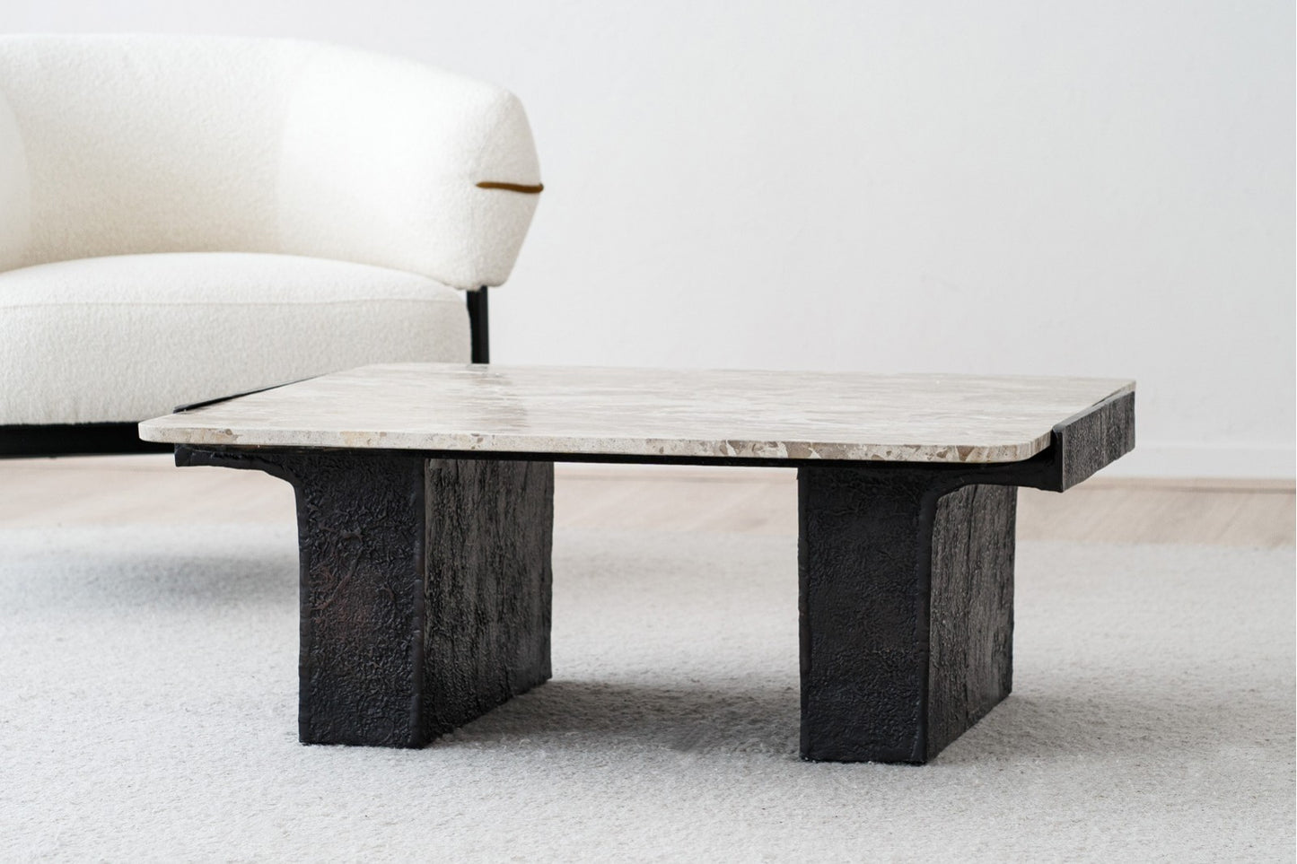 A modern Mesa de centro cuadrada de mármol 90×90×35 CM con acabado óxido y estructura metálica negra, situada sobre una alfombra clara cerca de un sillón tapizado blanco.