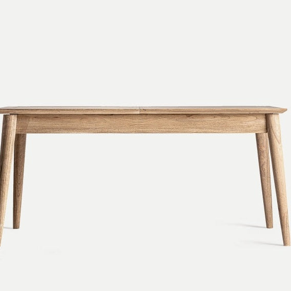 La mesa de comedor extensible en madera mindi Nyry presenta un diseño elegante con un acabado ligero y cuatro patas en ángulo, sobre un fondo liso para resaltar su diseño contemporáneo.