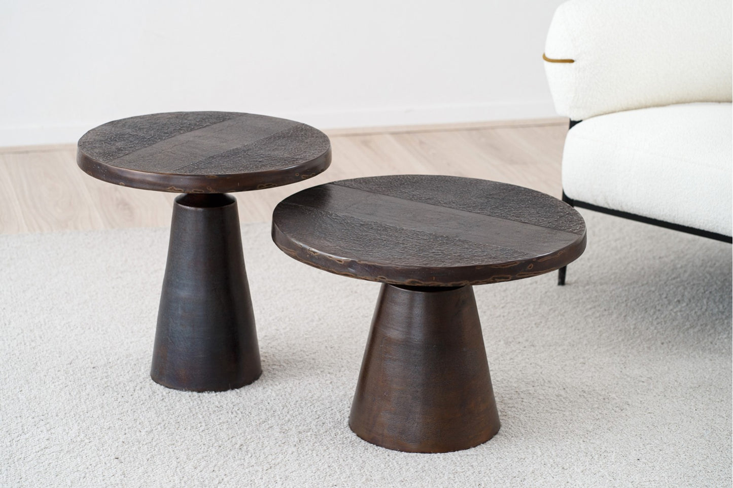 Dos mesas auxiliares redondas de metal BRONZ, 58×44 y 50×51 cm, con acabado bronce envejecido y estilo contemporáneo, aportan un toque moderno sobre una alfombra clara junto a un sofá tapizado en blanco.