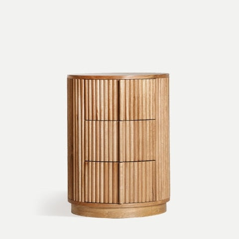 La mesita de noche en madera de paulownia Skagen2 es una mesa auxiliar cilíndrica de madera con listones verticales y tablero liso, con tres cajones. Con un diseño nórdico minimalista, está fabricada en resistente madera de paulownia y complementa cualquier habitación con elegancia.