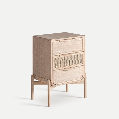 La Mesita de noche en madera de fresno Weurtz, un mueble de madera con tres cajones, uno de ellos adornado con ratán tejido, se yergue elegantemente sobre cuatro patas sobre un fondo sencillo. Sus tonos sutiles y líneas limpias personifican la esencia del diseño escandinavo.