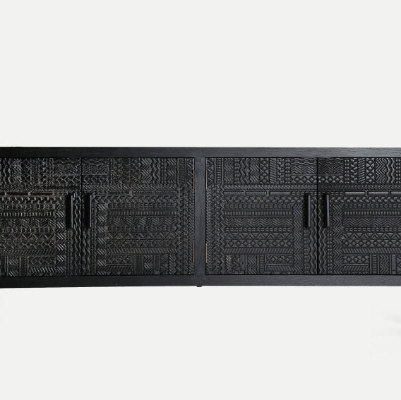 El mueble TV en fresno negro con puertas Antrim es un aparador negro elaborado con elegante madera de fresno negra con intrincados tallados geométricos en las puertas y cuatro elegantes manijas, lo que lo convierte en una pieza elegante que se destaca maravillosamente sobre un fondo claro.