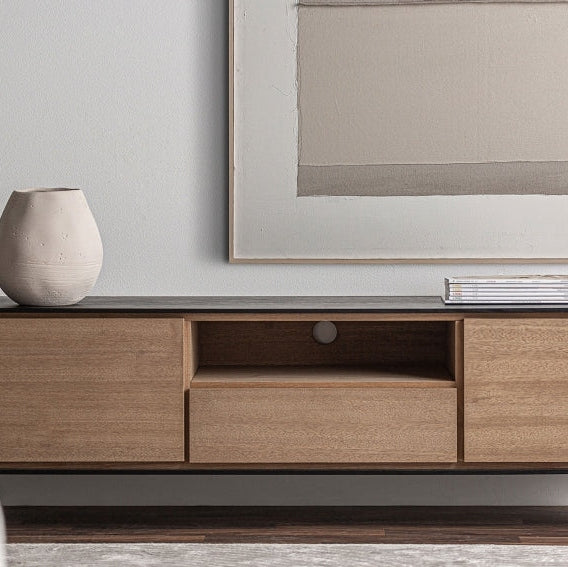 El mueble TV en madera DM y hierro Brussa de diseño de estilo industrial está adornado con un jarrón redondo a la izquierda y una gran pintura abstracta encima, sobre una pared blanca prístina.