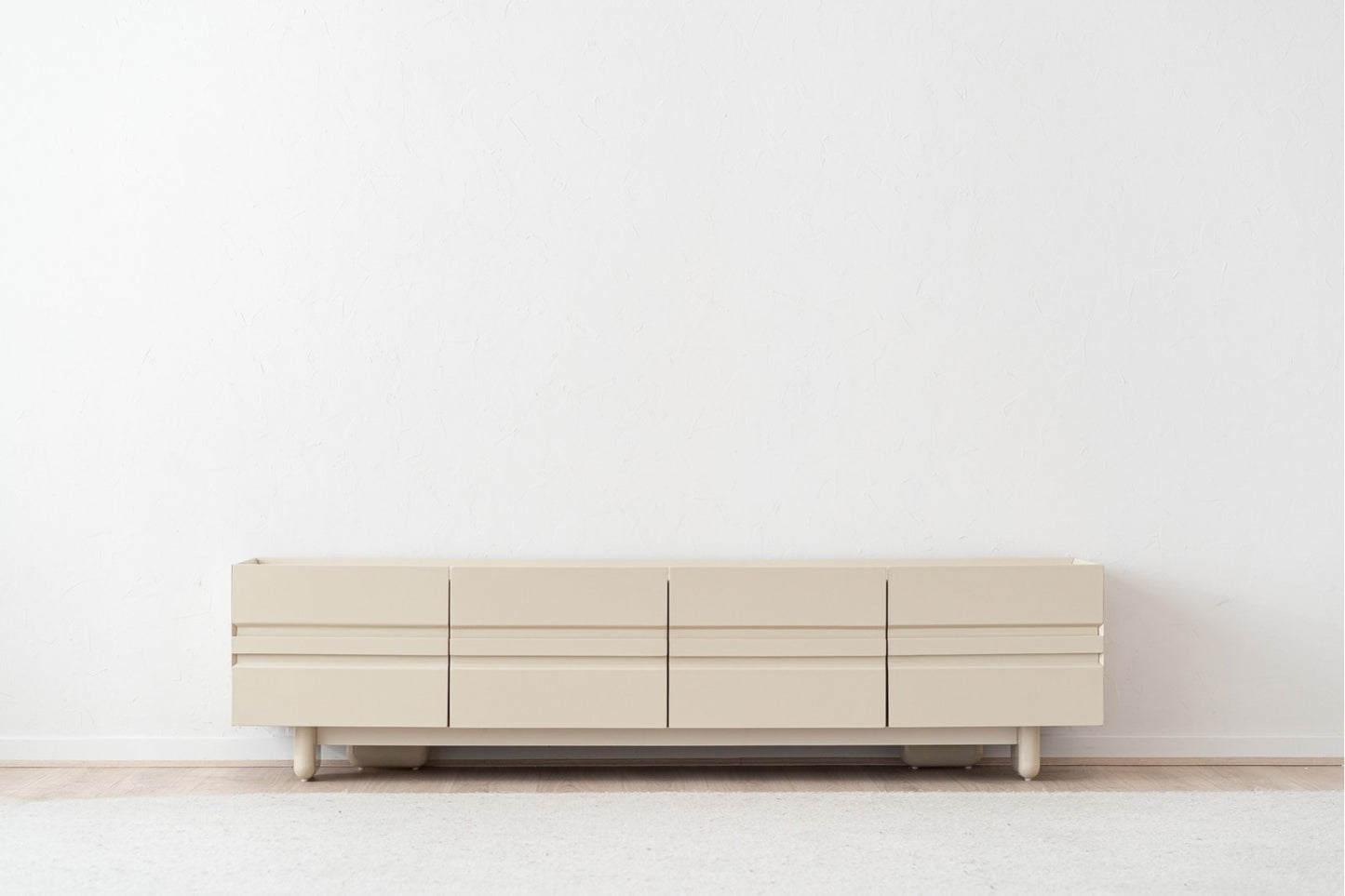 Un moderno mueble de TV beige brillante con acabado cerámico gris mate (200×43,5×50 cm) se alza contra una pared blanca sobre un suelo de madera clara y una alfombra, perfecto como mueble de salón minimalista.