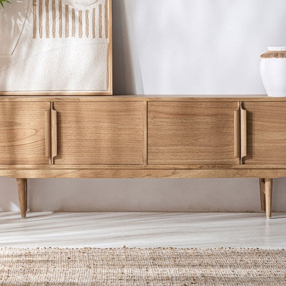 El mueble de TV NYRY en madera mindi, con tres puertas y patas cónicas, encarna el estilo nórdico. Colocado sobre un suelo claro junto a obras de arte en la pared y un jarrón blanco con rayas marrones, combina a la perfección elegancia y funcionalidad.
