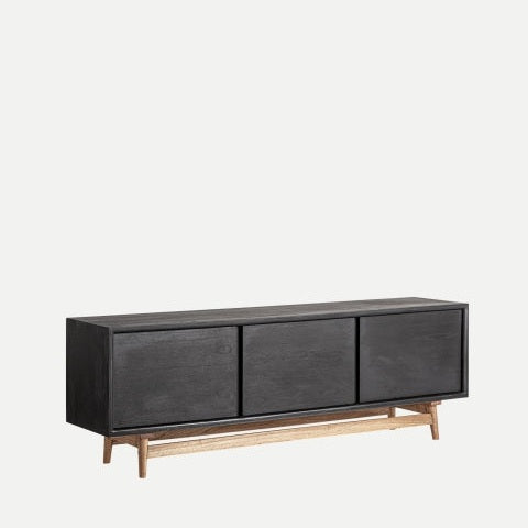 El mueble TV de madera de mindi negro Thiers es un aparador contemporáneo de madera negra con tres cajones sobre una base de madera clara, que refleja su elegante diseño sobre un fondo blanco liso.