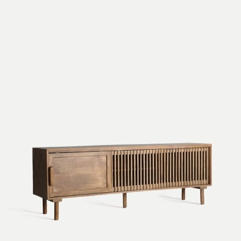El mueble para TV en madera de mango Trevoux cuenta con una puerta de armario en el lado izquierdo y listones verticales en el lado derecho, sostenidos por cuatro patas cortas. Su diseño sencillo pero elegante evoca un estilo nórdico moderno y está fabricado con madera de mango de alta calidad.