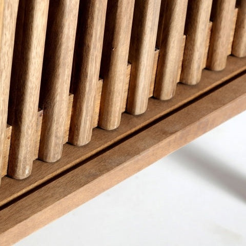 Primer plano de las lamas verticales de madera del Mueble TV de mango Trevoux, proyectando sombras sobre una superficie clara inferior. Este detalle captura la esencia del estilo nórdico moderno.