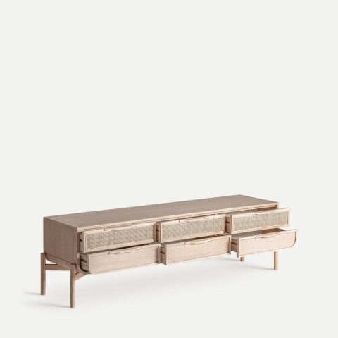 El Mueble TV de madera de fresno y ratán Weurtz, fabricado en elegante madera de fresno, cuenta con cuatro cajones parcialmente abiertos. Con su diseño minimalista y estilo contemporáneo, este aparador se alza elegantemente sobre cuatro patas.