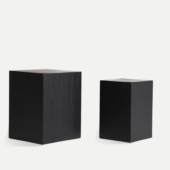 Peana Amilly, un juego de mesa auxiliar cuadrada minimalista, incluye dos pedestales de madera negra de diferentes alturas elaborados con elegante madera de abeto sobre un fondo claro.