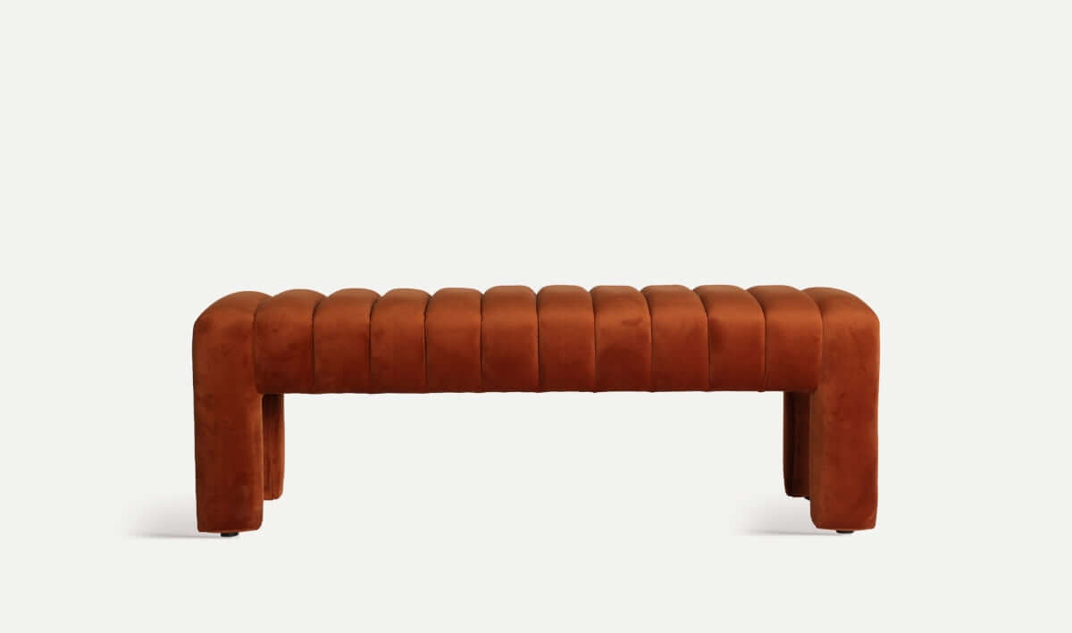 El pie de cama moderno HALLE presenta un tapizado de terciopelo ámbar con un diseño acanalado y patas robustas, y mide 127×43×43 cm, sobre un fondo blanco liso.