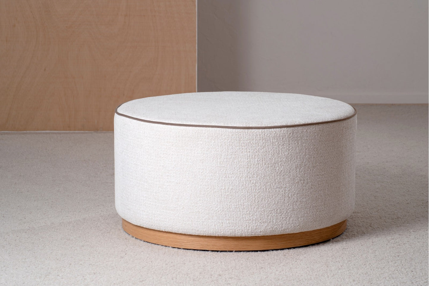 El Puf redondo tapizado en marfil y topo 80×80×41 CM, con base de fresno natural, de estilo contemporáneo ADA, es un elegante asiento auxiliar en la alfombra de esta sala minimalista.