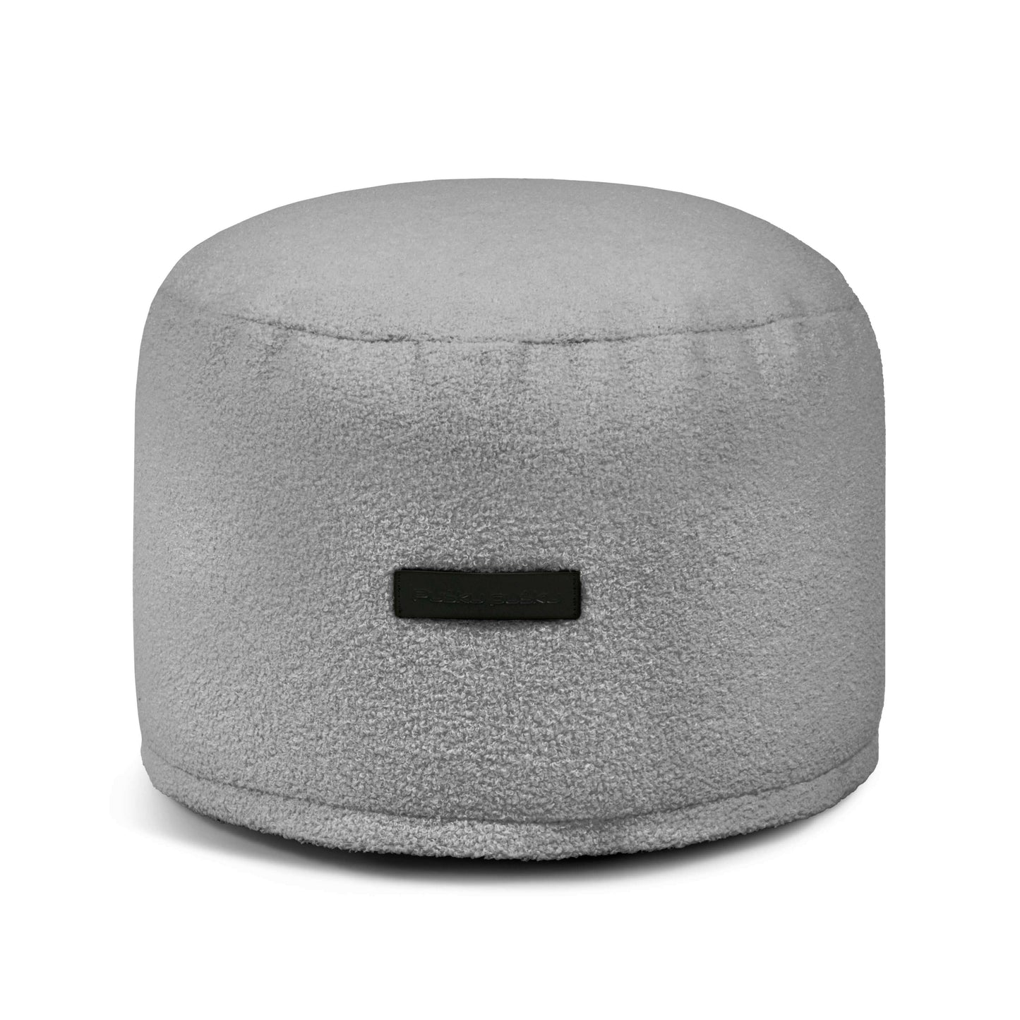 El Puff redondo de borreguito 40×40×30 cm MINI TEDDY es un asiento compacto y ergonómico en gris claro, ideal para dormitorio o salón, con suave textura y una pequeña etiqueta frontal.